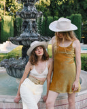 Summer Cowboy Hats for women. Two women posing in front of a fountain, one in a white outfit and the other in a gold dress.