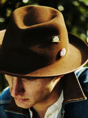 Model in a denim jacket wearing the Mick wool felt fedora in Brown.